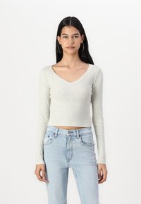 Világosszürke, hosszú ujjú, V-nyakú crop top, bordás anyagból, világoskék, magas derekú farmernadrággal párosítva.