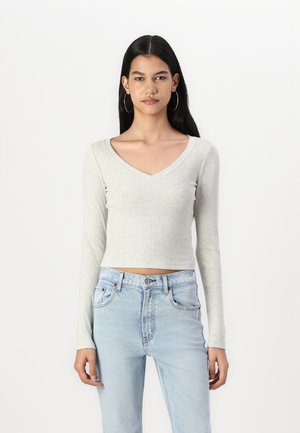 Világosszürke, hosszú ujjú, V-nyakú crop top, bordás anyagból, világoskék, magas derekú farmernadrággal párosítva.
