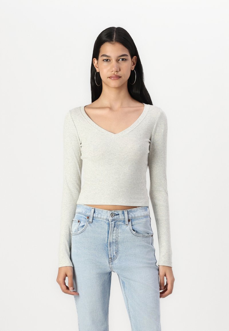 Világosszürke, hosszú ujjú, V-nyakú crop top, bordás anyagból, világoskék, magas derekú farmernadrággal párosítva.