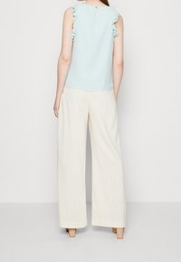 Top senza maniche di un blu chiaro con spalle arricciate e un dettaglio di bottoni sul retro. Abbinato a pantaloni larghi color crema con sottili righe verticali.