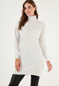 Lys grå turtleneck sweaterkjole med ribbede manchetter og kant, der har en blød tekstur og en let længere bagdesign.