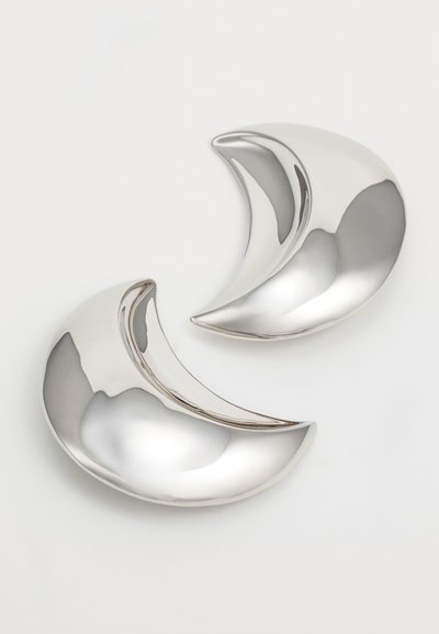 Objets décoratifs en forme de croissant argenté avec une finition polie, présentant des courbes lisses et des surfaces réfléchissantes, disposés étroitement les uns à côté des autres.