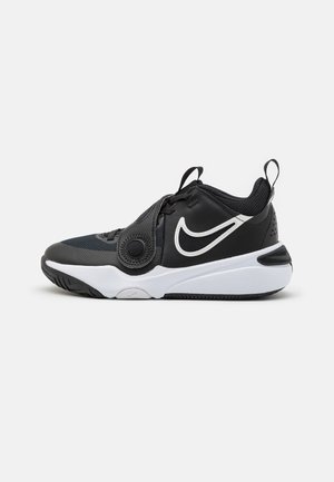 Chaussure de sport noire avec un dessus en maille et synthétique, accents blancs, une boucle circulaire et une semelle en caoutchouc avec une texture antidérapante.