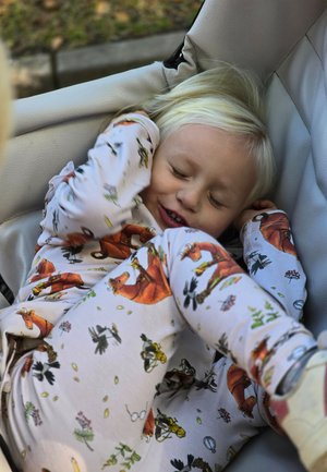 Lapsi vaaleissa pyjamissa, joissa on eläin- ja kukkakuoseja, makaa mukavasti vaalealla pinnalla. Lapsella on vaaleat, vaaleanblondit hiukset.