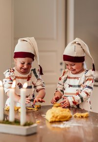 Kaksi lasta, jotka pukeutuvat beigeihin ja viininpunaisiin kärkitöppöihin, leikkivät keltaisella taikinalla. Heillä on päällään eläinprinttisiä, kuviollisia pitkähihaisia paitoja.