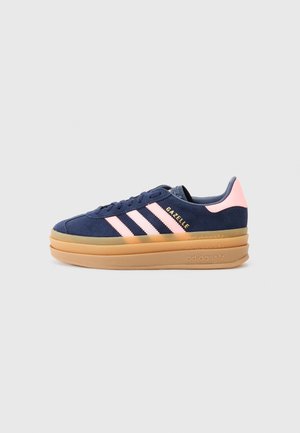 Mørkeblå Adidas Gazelle sneaker med lyserøde striber, lyserød hælflig og tyk lagdelt beige sål mod en lysegrå baggrund.
