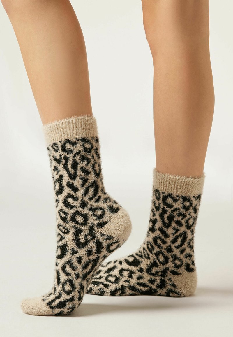 Leopardenmuster-Socken in Beige und Schwarz, aus weichem, strukturiertem Material. Mit einem dicken, gerippten Bündchen und einem plüschigen Körper.