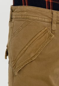 Khaki cargo kalhoty s texturovanou tkaninou, šikmou boční kapsou, pevným prošíváním a klasickým střihem, s pasem ve střední výšce.