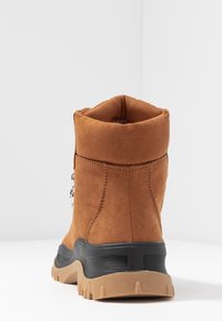 Bottine en daim marron avec un col rembourré, une semelle en caoutchouc noire et un détail de fermeture éclair sur le côté. Caractérisée par une finition texturée et une construction robuste.