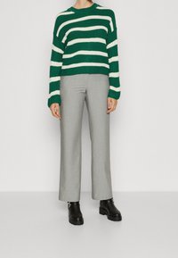 Maglione a righe verdi e bianche lavorato a maglia con scollo rotondo, abbinato a pantaloni a gamba larga grigio chiaro e stivaletti neri chunky alla caviglia.