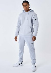 Set di felpa grigia chiara e pantaloni realizzati in tessuto morbido, con tasca frontale, cappuccio regolabile e tasche in stile cargo con accenti neri.