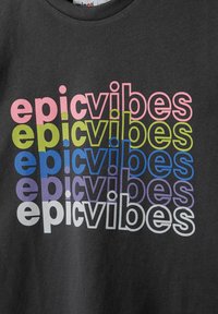 Fekete pamut póló, amelyen különböző színekben ismétlődő "epic vibes" szöveg található: rózsaszín, zöld, kék, lila és fehér; modern tipográfiai dizájn.