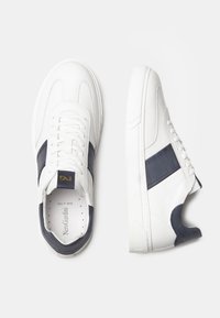 Sneakers bianchi in pelle con dettagli in suede navy, caratterizzati da una punta perforata, lacci piatti e suola in gomma. Design minimalista con marchio in rilievo.