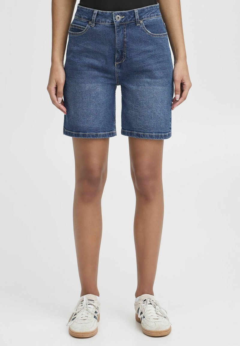 Denimshorts i blå bomull med rak passform, med bältesöglor, framfickor och uppvikta fållar. Bärs med vita sneakers.