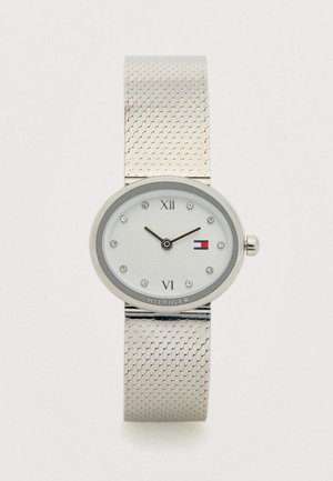 Montre en argent avec bracelet en maille, cadran ovale, marqueurs d'heure en cristal, chiffres romains aux positions 12 et 6, et un petit logo de drapeau sur le cadran.