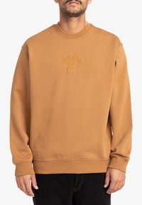 Sudadera marrón de algodón con cuello redondo y puños acanalados. Presenta un diseño de flores bordado en el centro.