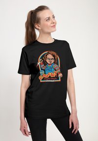 Černé tričko s barevným motivem panenky držící nůž a textem "Ahoj, jsem Chucky, chceš si hrát?". Jednoduchý design a bavlněná tkanina.