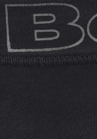 Tissu noir avec une surface texturée présentant un grand logo gris encadré dans une forme rectangulaire. Les coutures sont visibles le long des bords.