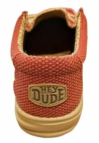 Röd vävd tygsko med tanfärgad gummi-sula. Har en cirkulär "HEY DUDE"-etikett på baksidan. Öppen design på toppen.