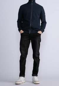 Marinblå ribbad ziptröja med hög krage, i kombination med svarta jeans och vita sneakers. Tröjan har texturerade horisontella linjer.