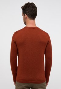 Maglione a maglia color ruggine con maniche lunghe e scollatura rotonda, caratterizzato da una texture liscia e un design aderente.