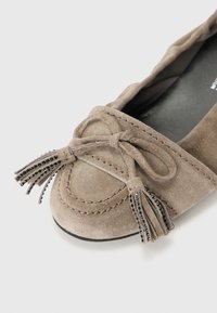 Ballerines en daim taupe à bout rond, ornées d'un nœud noué et de pampilles décoratives. Semelle en caoutchouc noir et détails cousus.