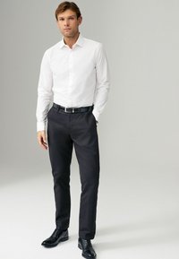 Chemise blanche à boutons, pantalon noir, chaussures en cuir. Coupe slim, tissu lisse, manches longues, col et une ceinture noire avec boucle en argent.