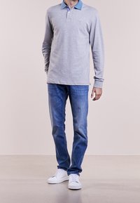 Polo grigio a maniche lunghe con colletto blu, abbinato a jeans blu e sneakers bianche. Tessuto dalla texture liscia e design aderente.