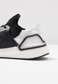 Czarno-białe buty sportowe z siateczkową cholewką, teksturowanym piętą i gumową podeszwą, z unikalnym plastikowym akcentem po boku.