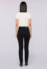 Pantalones ajustados negros con cintura alta, bolsillos traseros y un acabado suave. Combinados con una blusa blanca de manga corta.