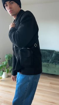 Crna torbica na rame s teksturiranom površinom i srebrnim patentnim zatvaračem, nošena preko crne jakne. Ima podesivi remen i elegantan dizajn.