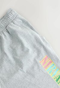 Pantalonii de trening gri au un elastic la talie și o grafică multicoloră "NIRVANA" imprimată pe coapsa stângă. Material moale, texturat.