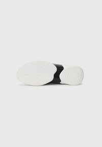 Sorte hvite og svarte joggesko med strukturert hvit gummi, med en avrundet form og rillet design for bedre grep.