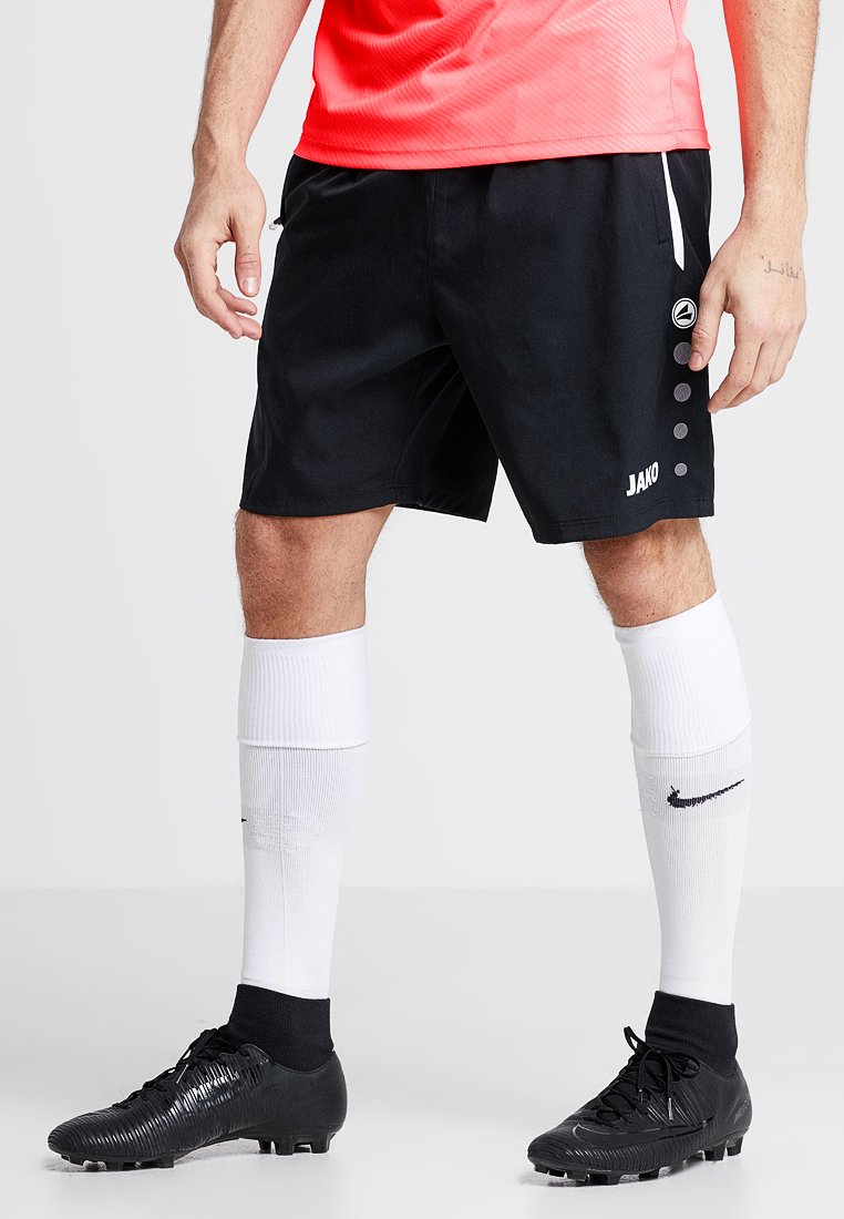 Schwarze Sportshorts mit einer glatten Textur, ausgestattet mit weißen Akzenten und sechs schwarzen Punkten an der Seite. Kombiniert mit weißen knielangen Socken.