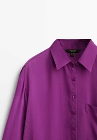 Chemise violette à manches longues avec boutons, col pointu et poche poitrine, vue de face sur fond blanc.