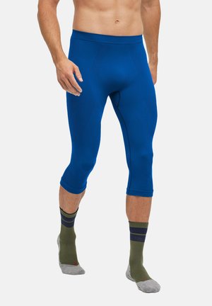 Blauwe compressie capri-broeken gemaakt van rekbaar materiaal met gestructureerde accenten en een aansluitend ontwerp. Draagt met groen en grijs gestreepte sokken.