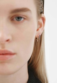 Pendientes de oro y plata con un diseño de aro, un charm colgante y pequeños acentos de color. Texturas suaves al contacto con la piel.