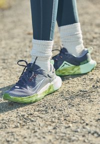 Zapatillas deportivas de malla azul marino con suelas verdes, que presentan acentos blancos, un tejido texturizado y detalles rojos en los cordones; combinadas con calcetines blancos de canalé.