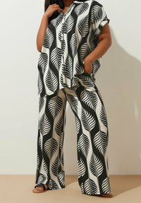 Camisa de gran tamaño con estampado de hojas en blanco y negro, pantalones a juego, mangas cortas, corte holgado y tela ligera; sandalias planas.