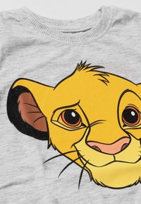 Close-up of a gray fabric with a printed cartoon lion cub face in yellow, orange, and black colors.