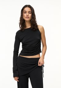 Haut noir à manches longues avec un design asymétrique, présentant une texture froncée sur un côté. Associé à des pantalons noirs drapés assortis.