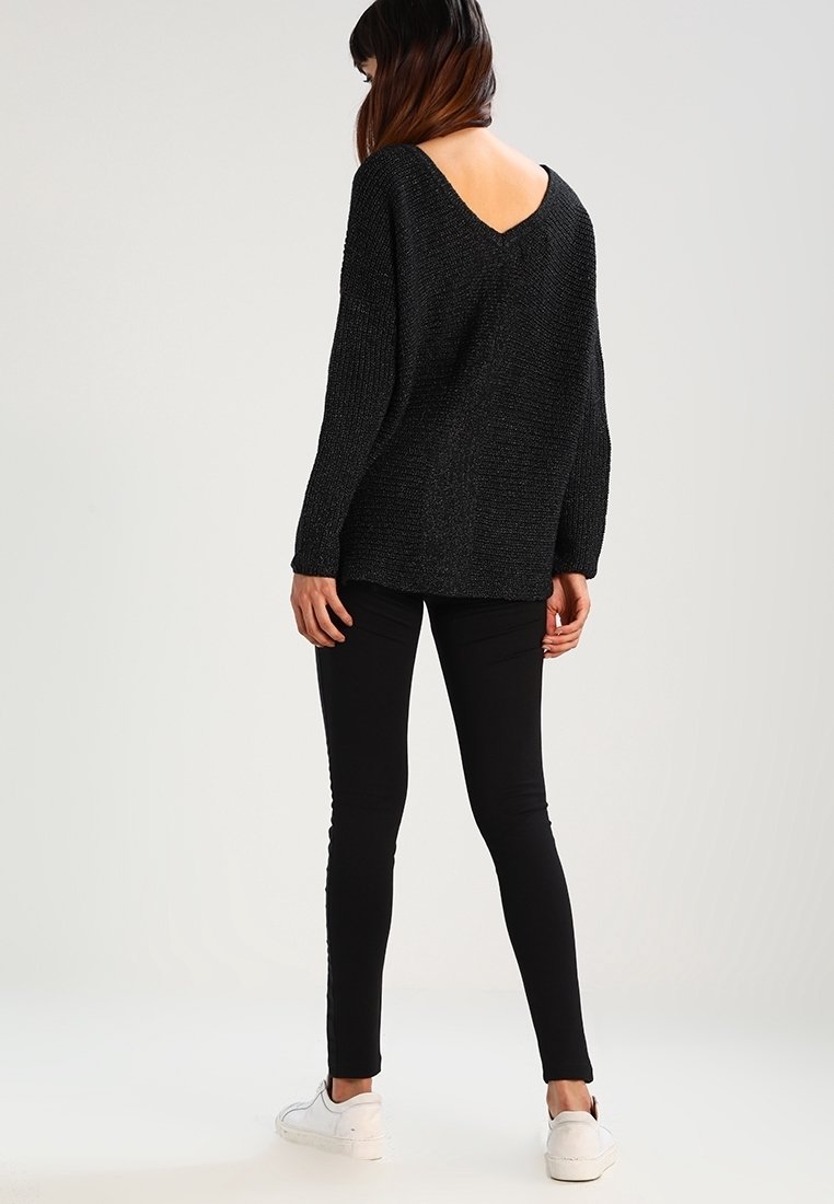 Pull en tricot noir avec un design décolleté en V, associé à un legging noir et des baskets blanches. La texture semble douce et ample.