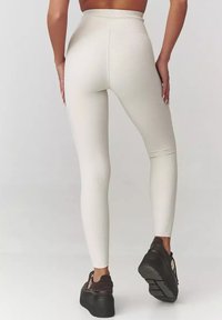 Legginsy z wysokim stanem, w kolorze ecru, dopasowany fason, z gładką fakturą i długością sięgającą kostek, w zestawie z ciemnymi butami na platformie.