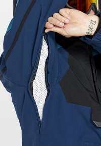 Blå jakke med lynlåsvindue og mesh-indvendig. Stoffet viser en kombination af solid blå og sorte detaljer.