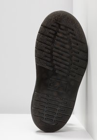 Czarna gumowa podeszwa buta z teksturowanym wzorem gripu i brandingiem. Projekt zawiera poziome i pionowe rowki dla lepszej przyczepności.