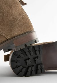 Bottines en suède marron, avec une semelle en caoutchouc noir robuste dotée d'un motif de relief et des accents en cuir.