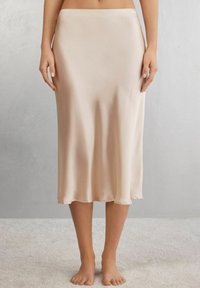 Jupe midi en satin de couleur beige clair, avec une texture lisse et une coupe A-line fluide, dotée d'un ourlet qui se courbe doucement.