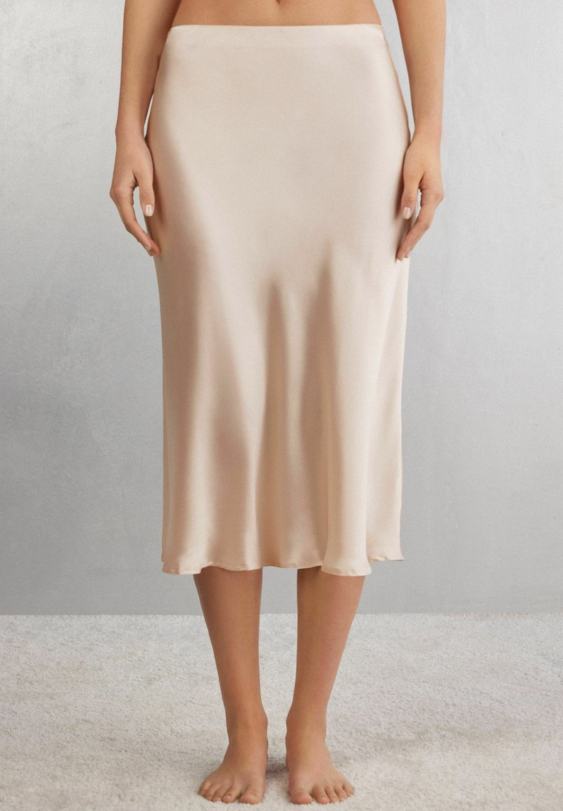 Jupe midi en satin de couleur beige clair, avec une texture lisse et une coupe A-line fluide, dotée d'un ourlet qui se courbe doucement.