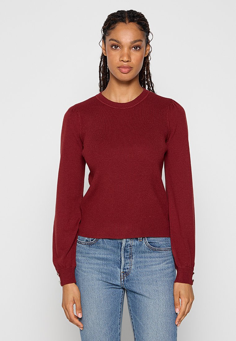 Bordeaux gebreide trui met lange, iets opbollende mouwen en een ribbelstructuur. Voorzien van een ronde halslijn en een aansluitende zoom. Geselecteerd met blauwe jeans.