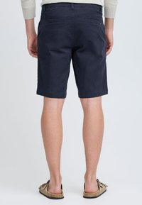 Shorts en coton bleu marine avec une coupe droite, deux poches arrière et des ourlets roulés, associés à des sandales beige clair.